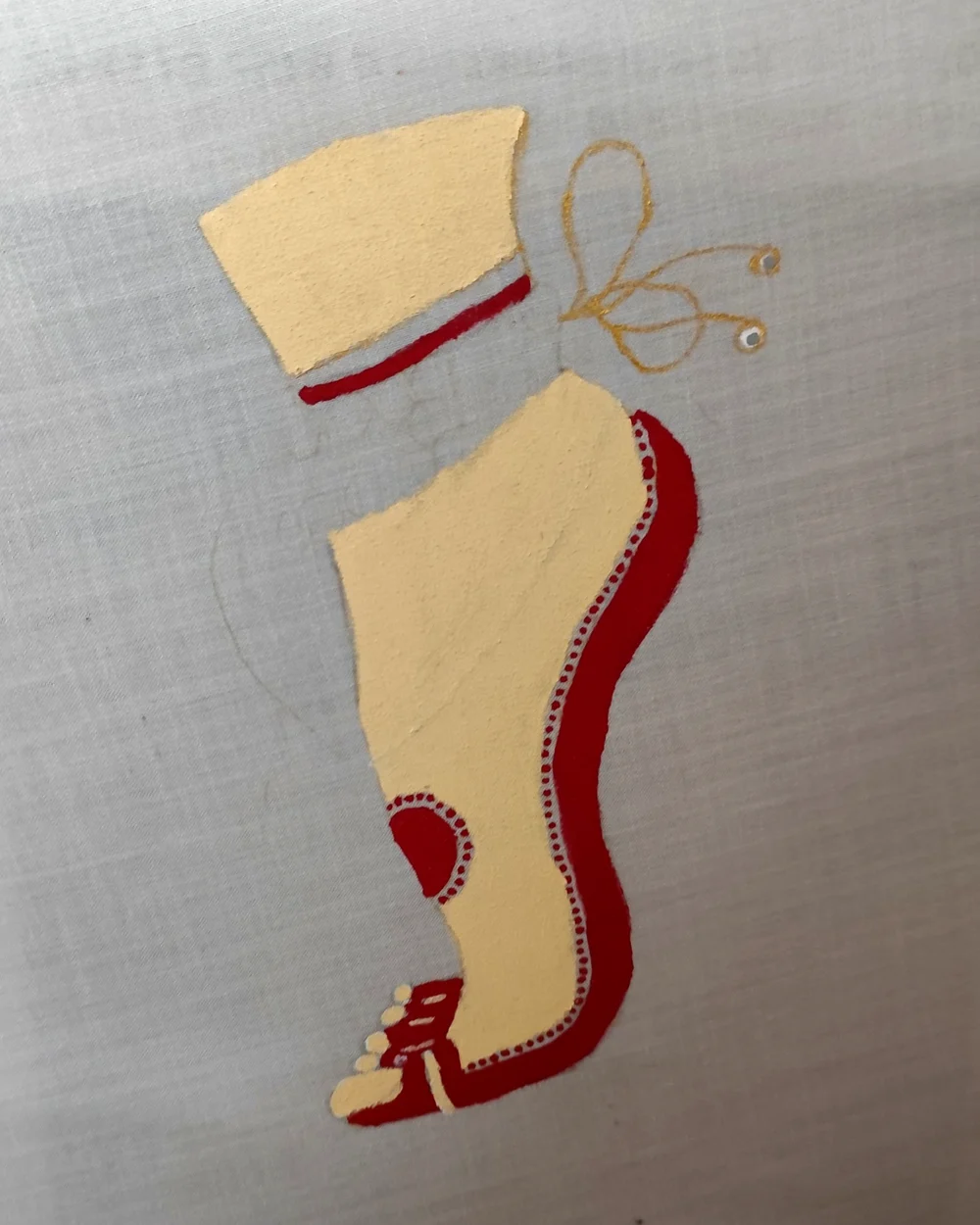 Fabric painting of a red and cream foot motif with fine dotted detail and gold thread